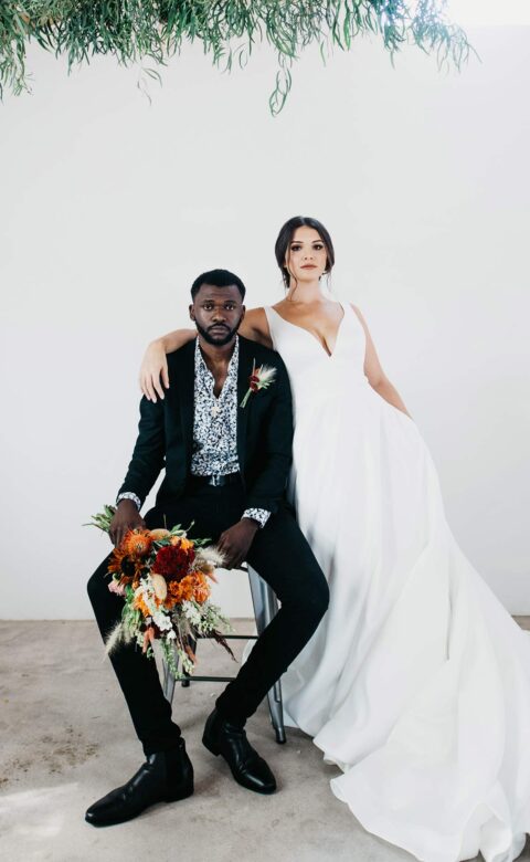 bride and groom sit on stool in white room