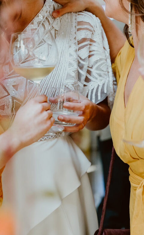 bride and two friends stand together holding glasses of white wine