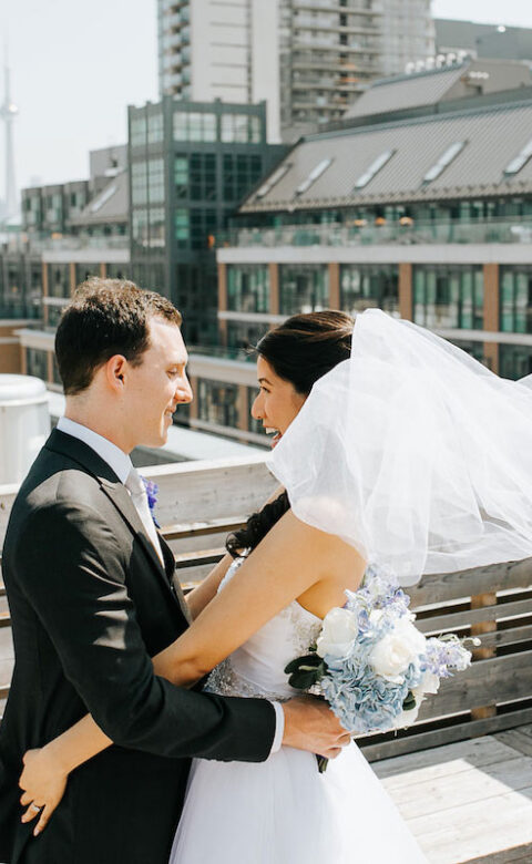 bride and groom smile while holding each other on rooftop