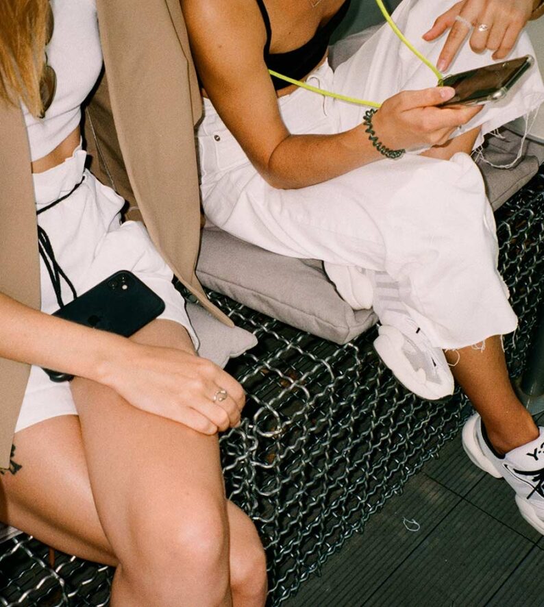 two people sitting on a mesh bench looking at a cellphone
