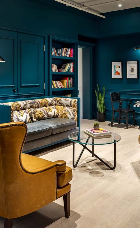 room with a bookcase and three couches with a small glass round table