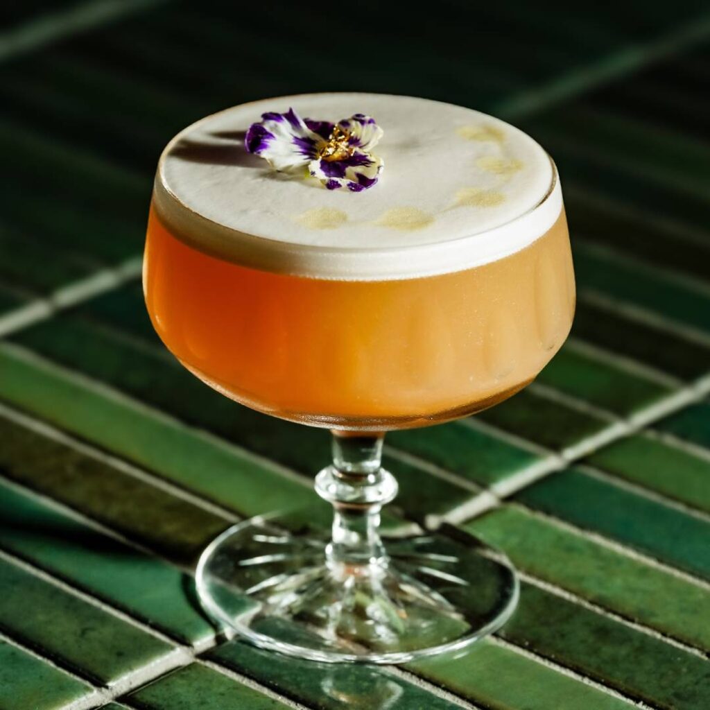 a cocktail with a creamy top garnished with a flower