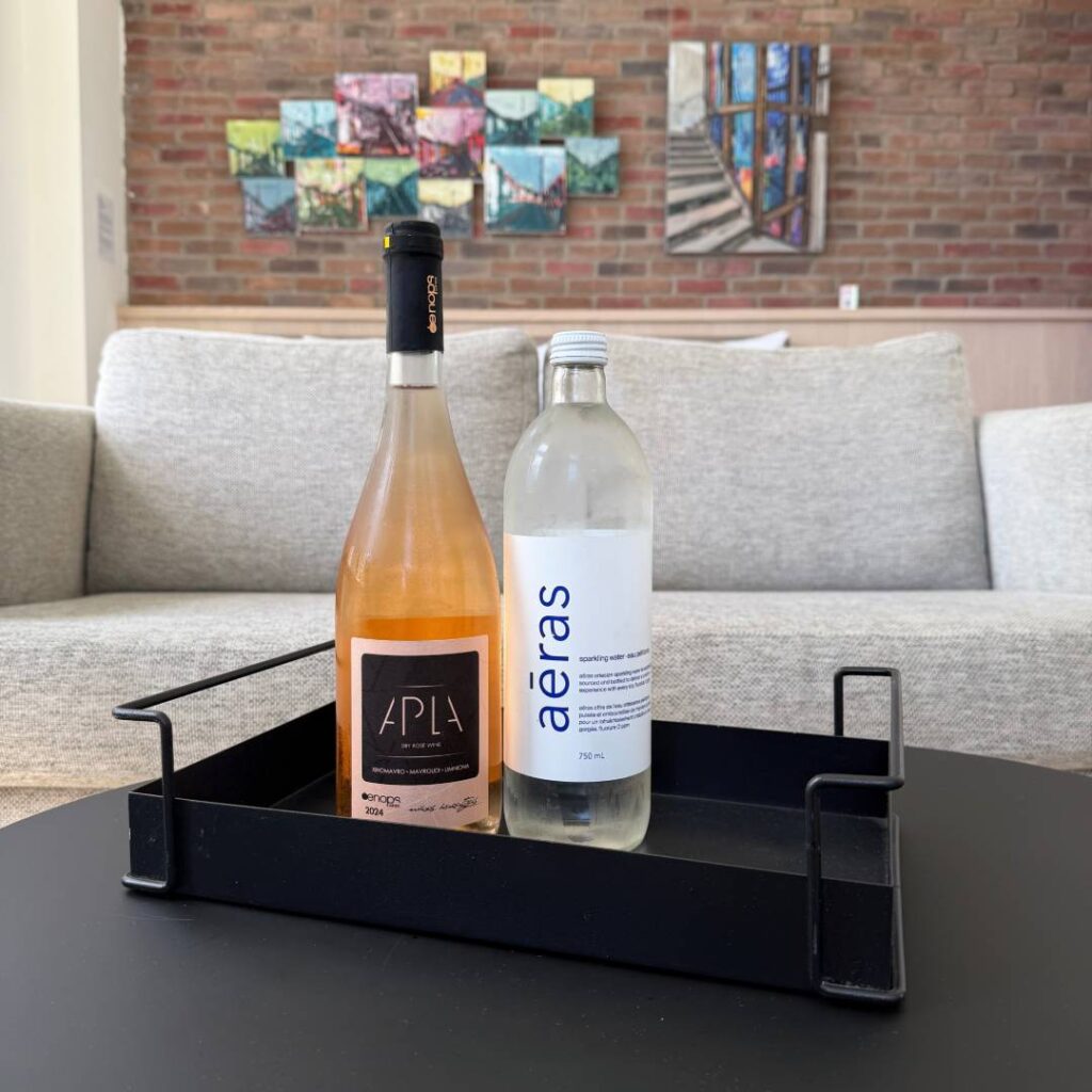 Bottle of APLA dry rosé wine and aēras sparkling water arranged in a black tray on a table, with lounge seating and colourful artwork in the background.